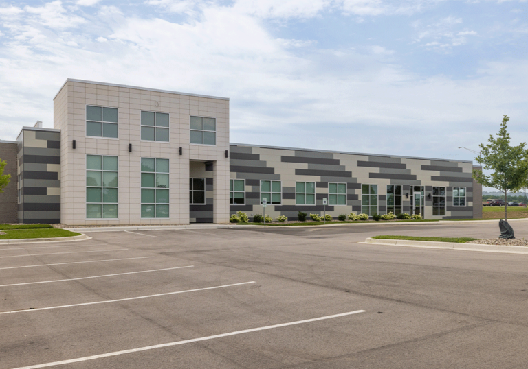 Modern, single-story commercial building with light and dark gray stripes, large windows, and an empty parking lot.