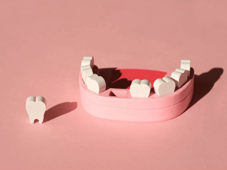 A pink dental model with white heart-shaped teeth on a pink background. One tooth is placed outside the model.